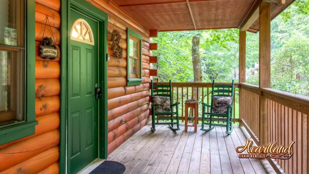 A cabin with a green door, a porch with two rocking chairs, and a view of the forest.