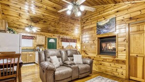 A cozy cabin interior with a leather sofa, wooden walls, a dining area, and a fireplace.