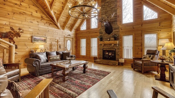 A log cabin interior with a fireplace, wooden walls, a chandelier, and a mounted moose head.