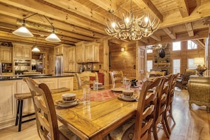 A wooden cabin interior with a dining area, kitchen, and a chandelier.