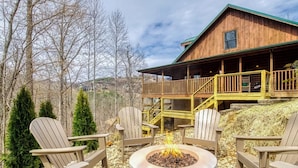 A wooden cabin with a stone fire pit and Adirondack chairs.