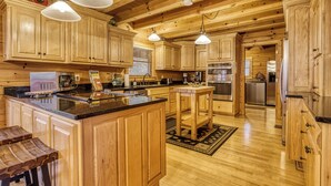 A wooden cabin interior with a kitchen featuring wooden cabinets, a central island, pendant lighting, and a built-in oven.