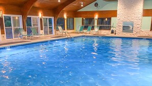Une piscine intérieure à eau claire, dotée de chaises longues et d’un mur en pierre.