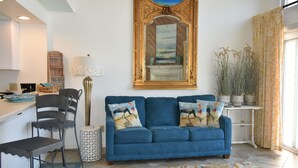 Un salon avec un canapé bleu, un tapis à motifs, un grand lampadaire et un grand miroir doté d’un cadre décoratif.