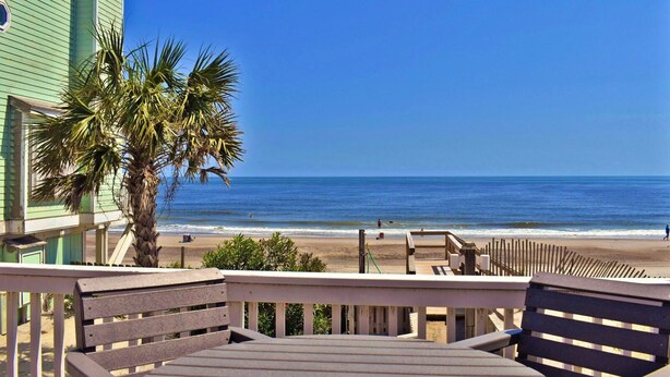 Une vue sur la plage depuis un balcon agrémenté de meubles en bois et d’un palmier.