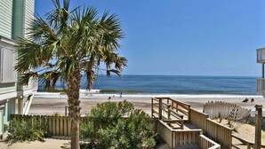 Une propriété située en bord de mer, dotée d’une terrasse en bois, d’un palmier et offrant une vue sur l’océan.