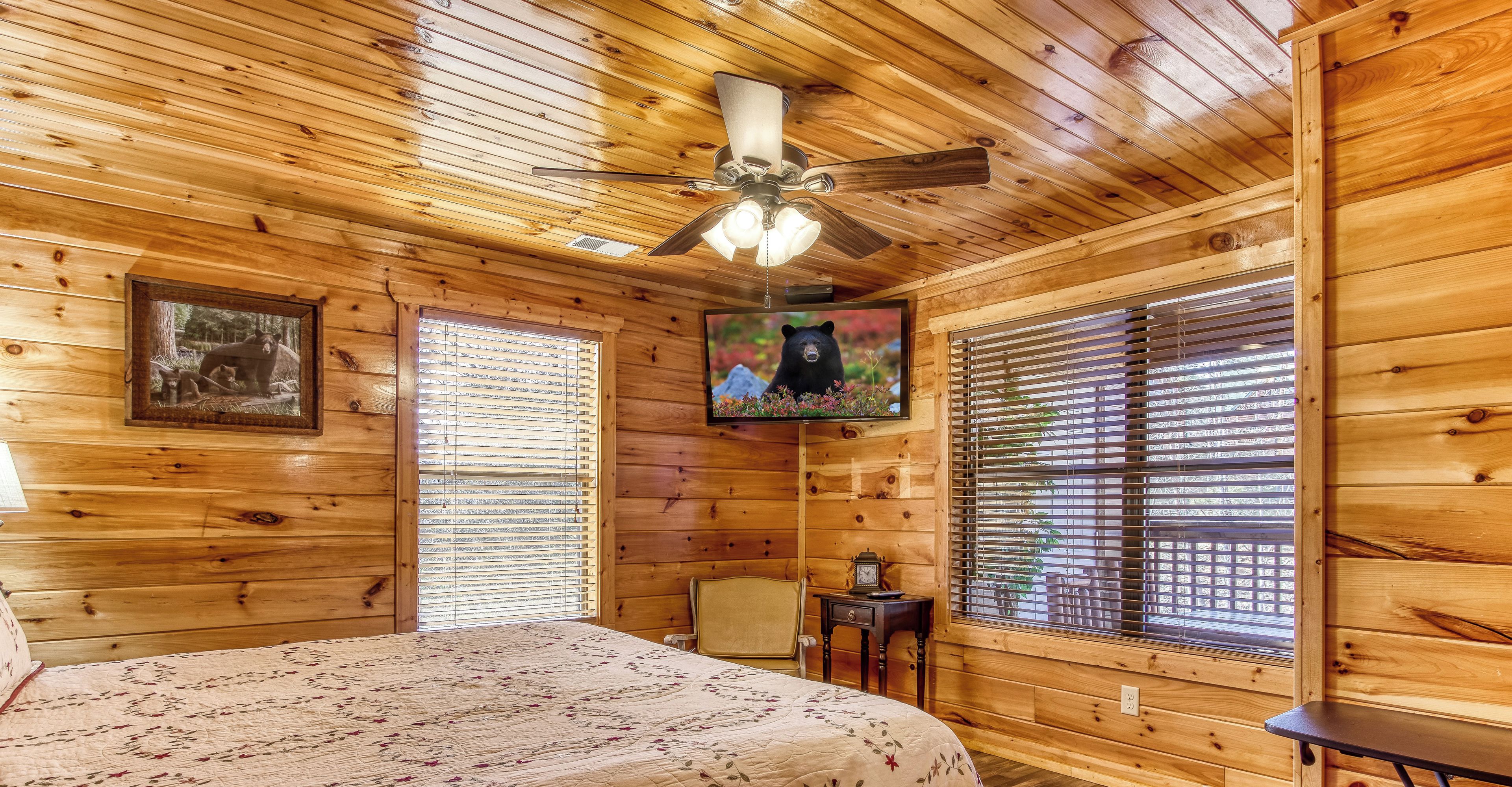 Dormitorio de una cabaña de madera con cama, ventilador de techo, televisor y paredes de madera.