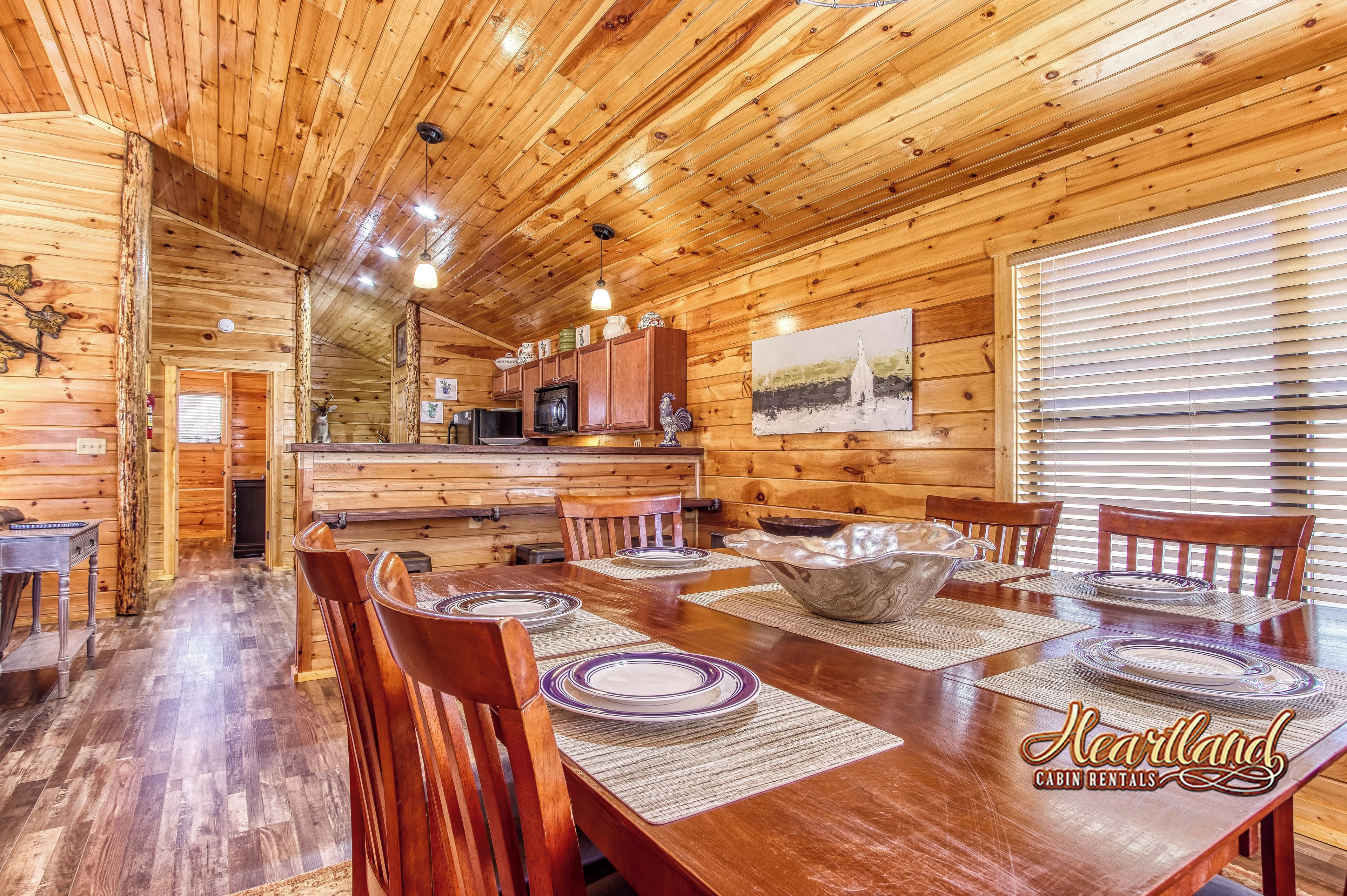 L’intérieur d’un chalet en bois comprend un coin repas, une cuisine et une grande fenêtre équipée de stores.