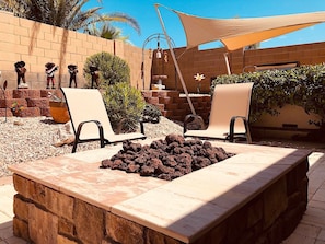 Un patio al aire libre con dos sillones de descanso, un hogar para fuego y un muro de ladrillo con adornos.