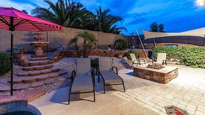Un patio con una fontana in pietra, poltrone relax e zona piscina.