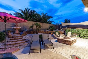 A patio with a stone fountain, lounge chairs, and a pool area.
