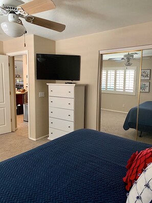 Un dormitorio con cama, televisor montado en la pared, armario y ventilador de techo.