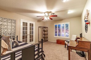Une chambre à coucher comprenant un lit, une armoire, un bureau, une chaise, une fenêtre et un ventilateur de plafond.