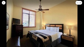 A hotel room with a bed, a nightstand, a lamp, a television on a dresser, and a ceiling fan.