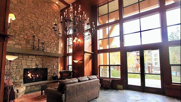 A spacious room with a stone fireplace, leather sofa, and large windows offering a view of the outdoors.