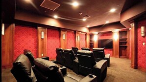 A theater room with rows of leather recliner seats, red patterned walls, and a carpeted floor.