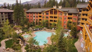 A hotel with a pool surrounded by trees and a mountainous backdrop.