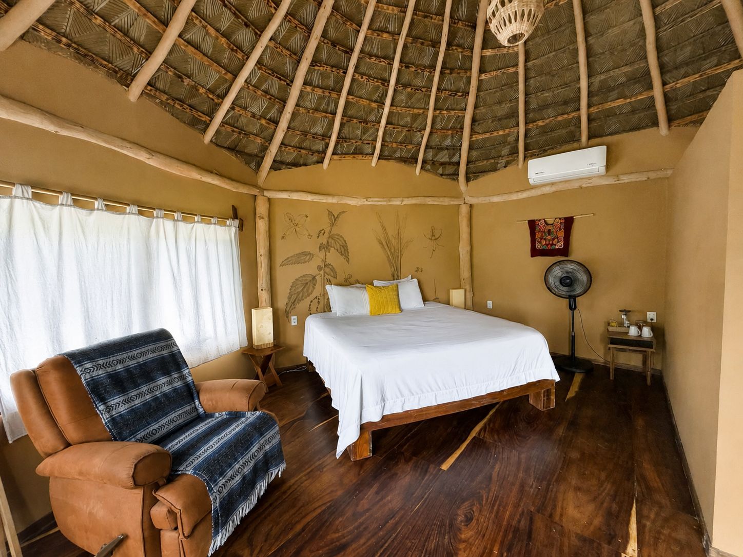 A room with a bed, a chair, a fan, and a wall-mounted air conditioner.