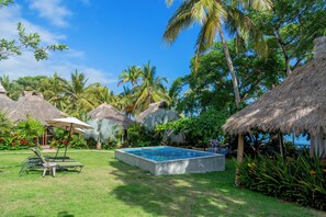 A pool surrounded by thatched-roof structures, lush greenery, and a clear blue sky. - Amaca Beach Retreat - Puerto Vallarta South Shore (Quimixto)