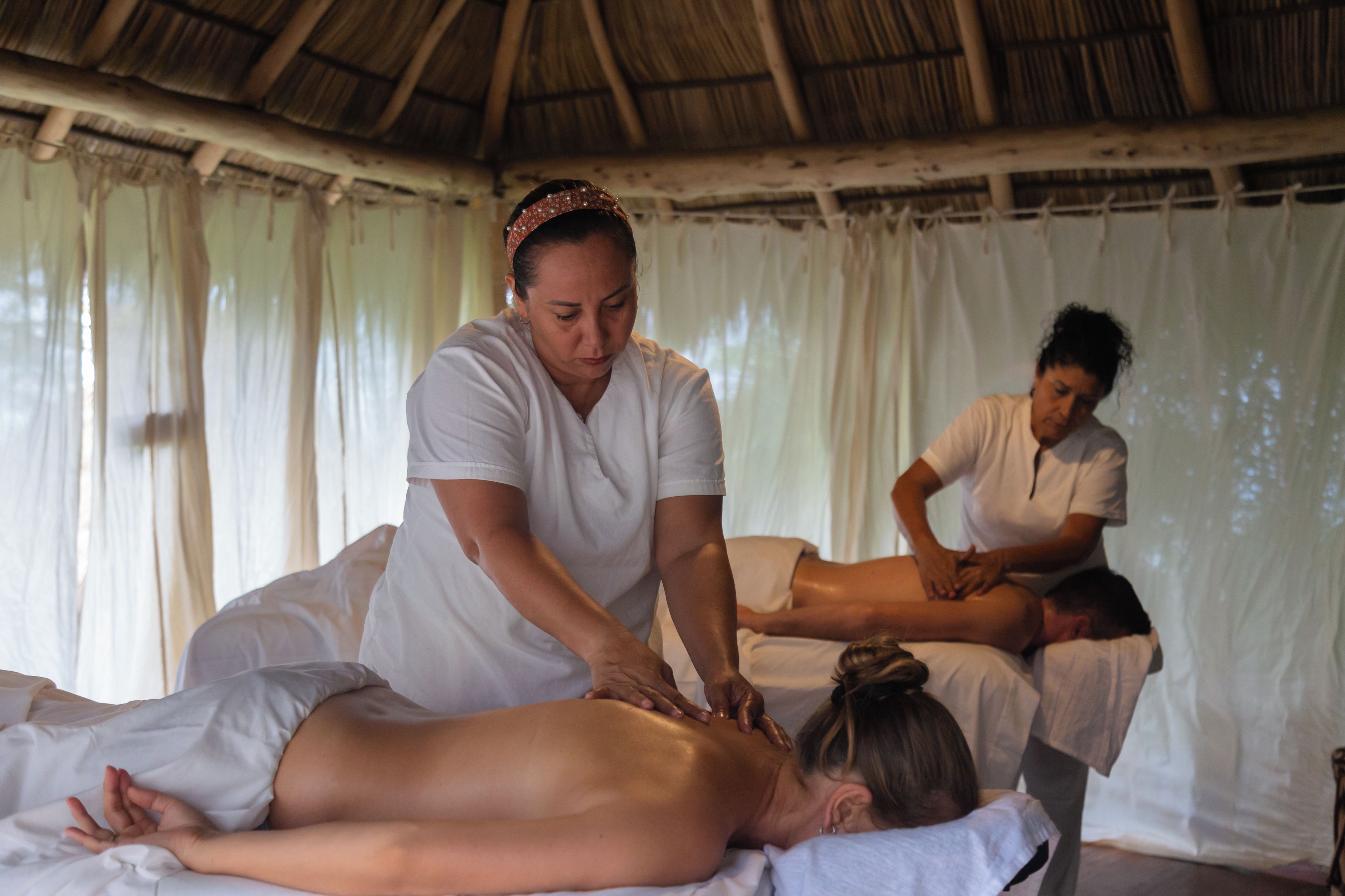A massage therapy session in a room with a thatched roof and white curtains.