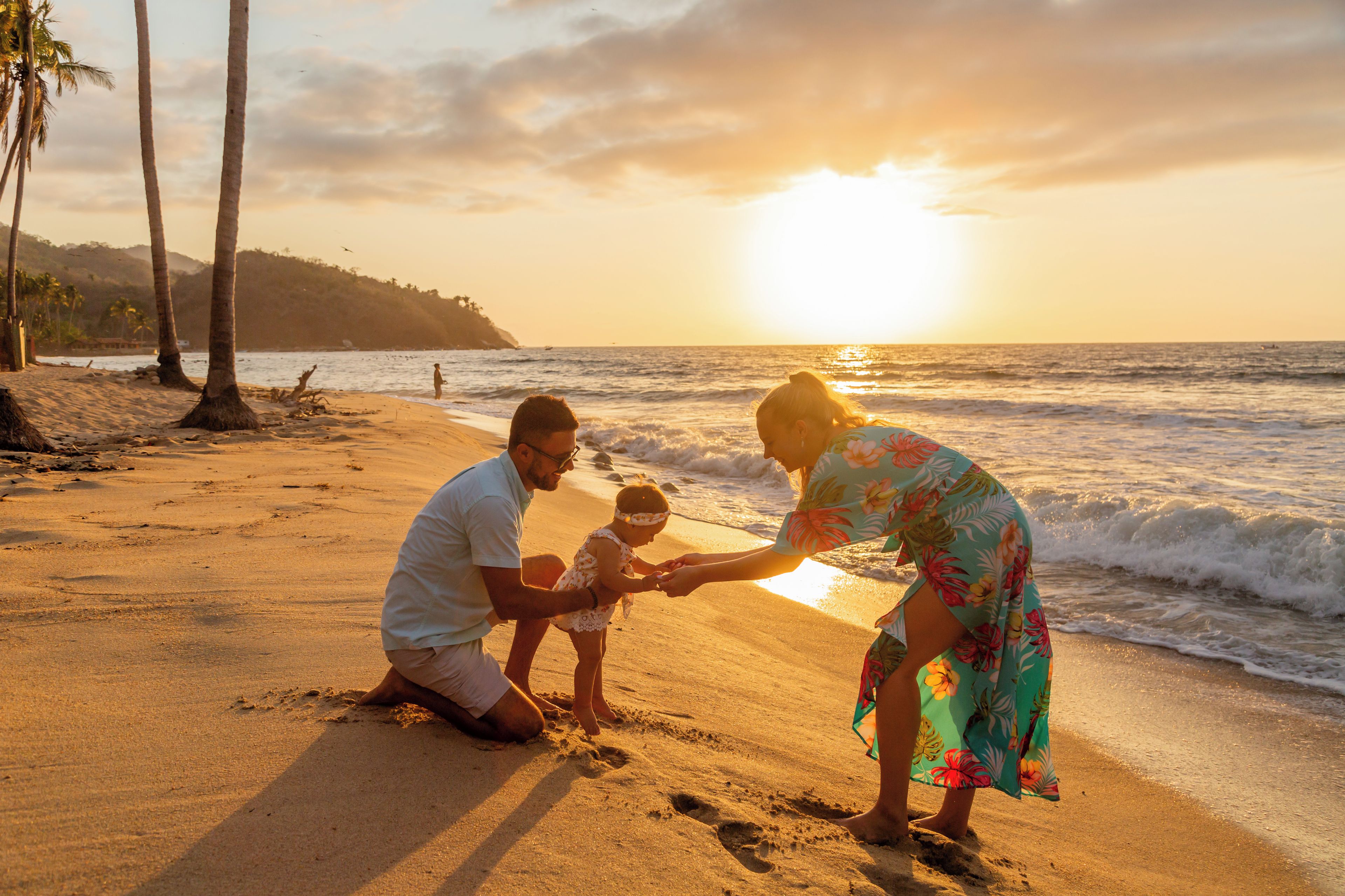 Eine Familie an einem sandigen Strand, im Hintergrund das Meer und ein Sonnenuntergang.