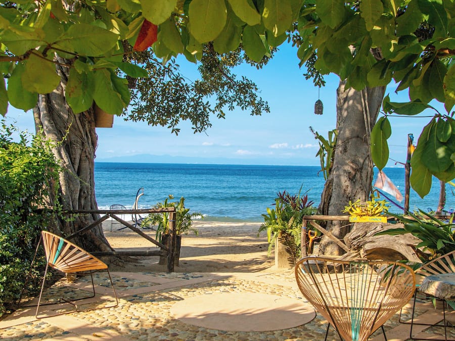 Un patio frente a la playa con vistas al océano, suelo de piedra y mobiliario exterior.