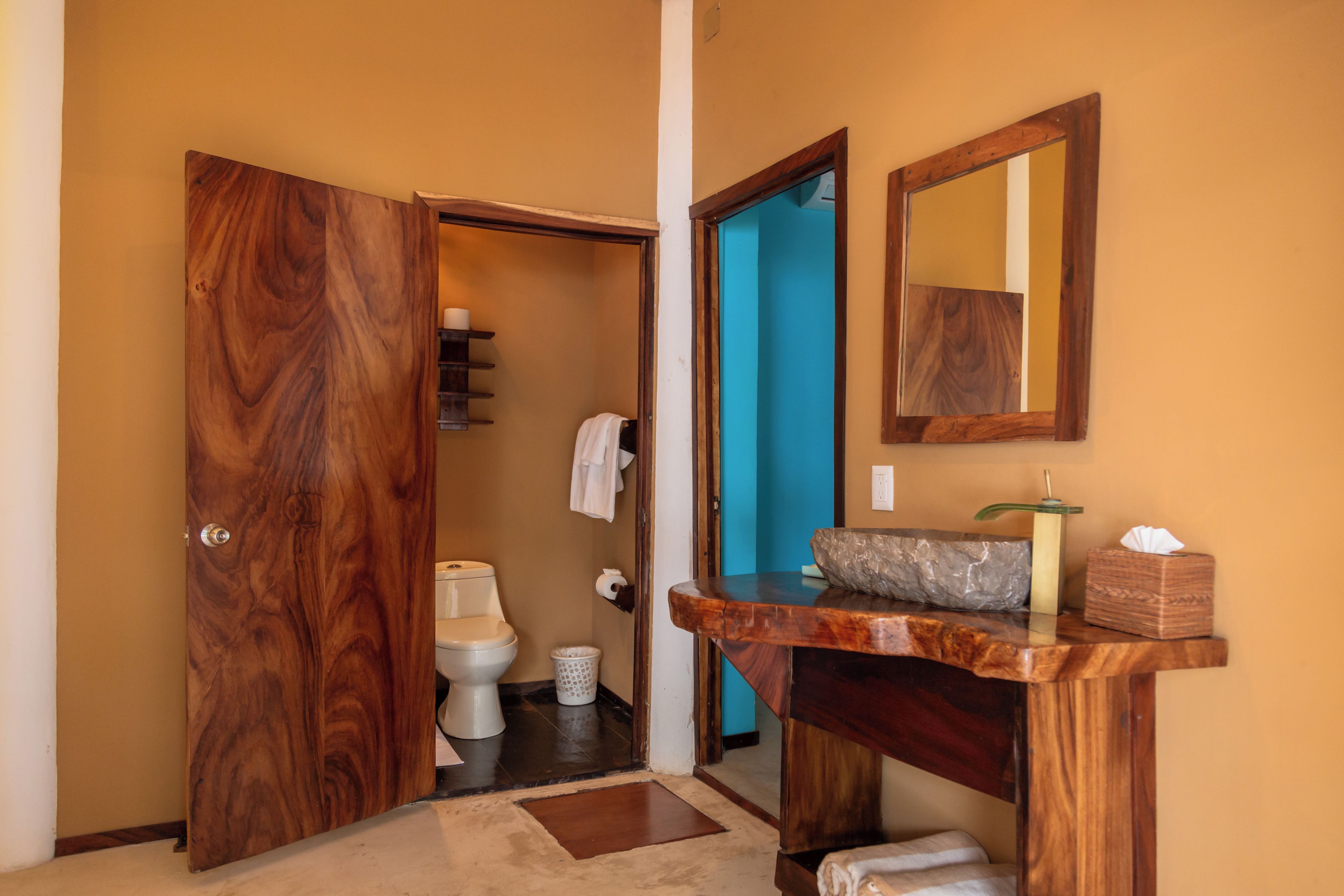 A bathroom with a wooden door, a toilet, a sink with a marble countertop, and a mirror.