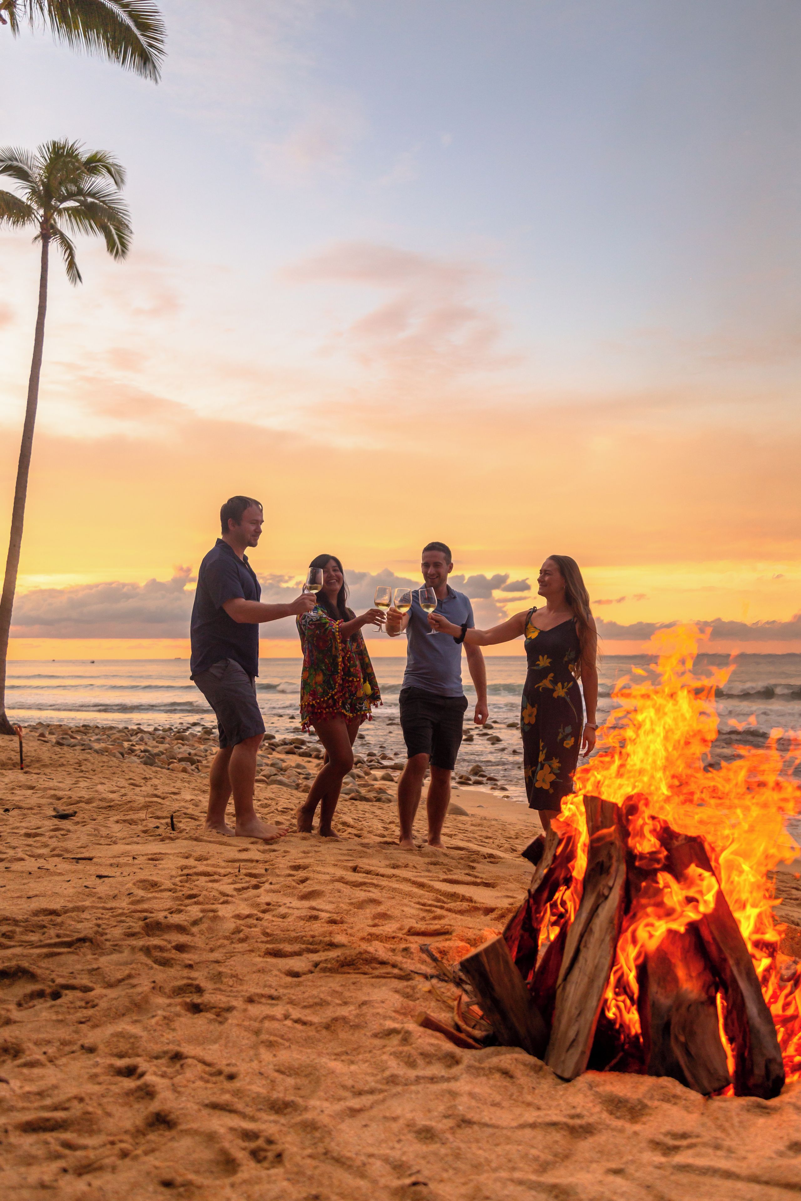 A group of people around a campfire on a beach with a sunset in the background.