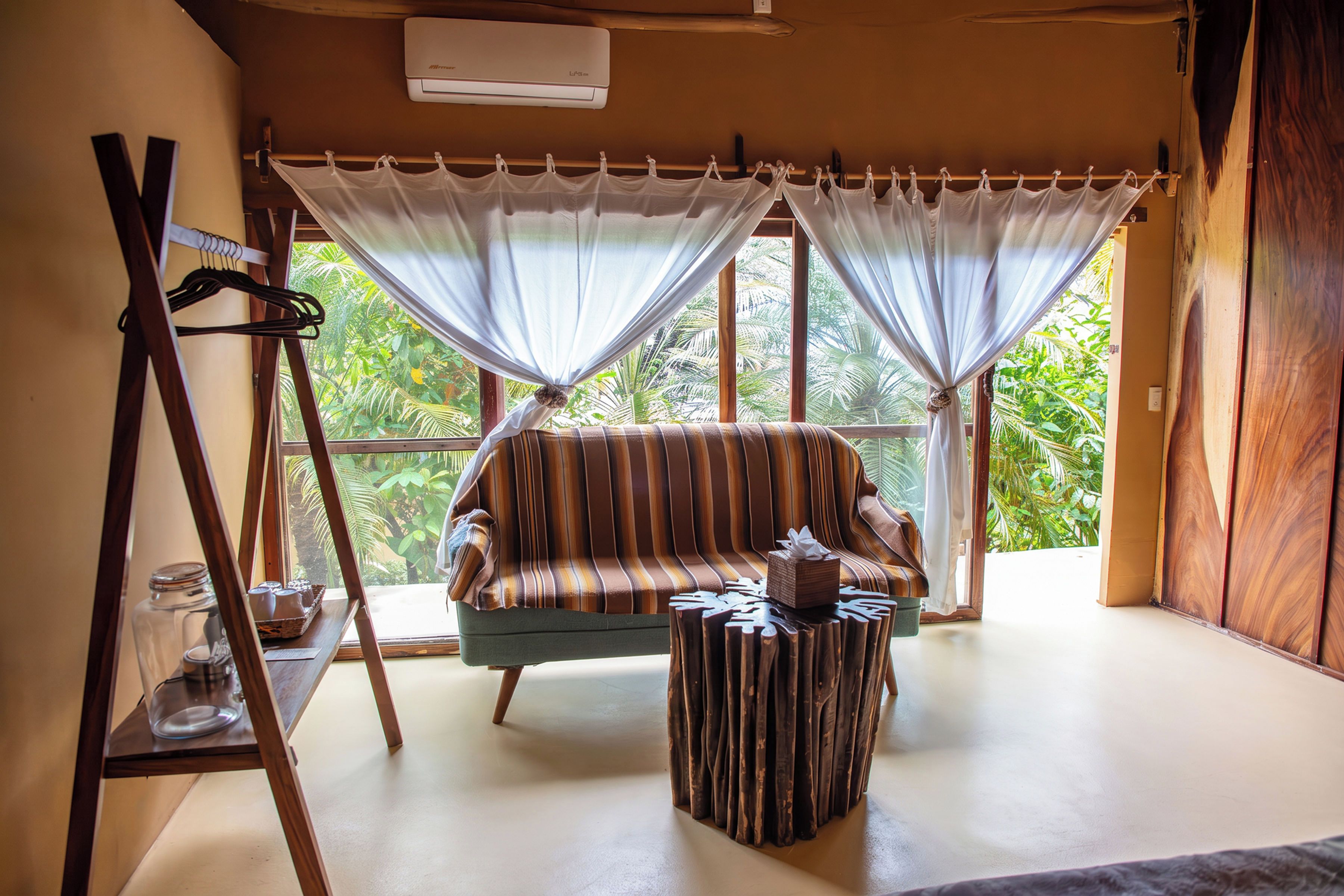 A room with a striped sofa, a small wooden table, and a large window with curtains.