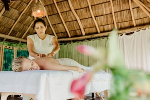 A massage therapy session in a room with a thatched roof and green curtains.