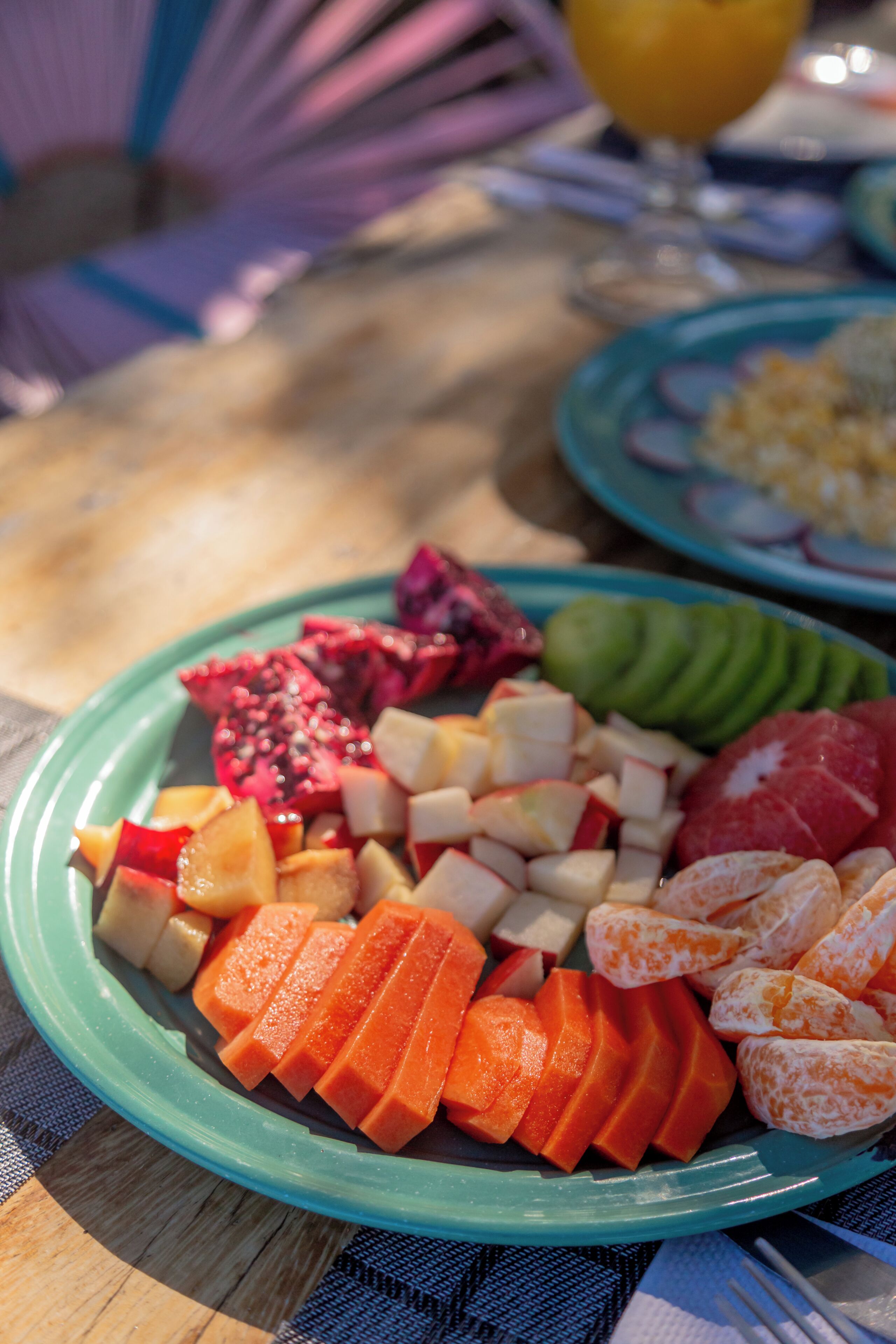A table with a plate of sliced fruits and vegetables, a glass of orange juice, and a plate with eggs and red onions.