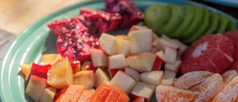 A table with a plate of sliced fruits and vegetables, a glass of orange juice, and a plate with eggs and red onions.