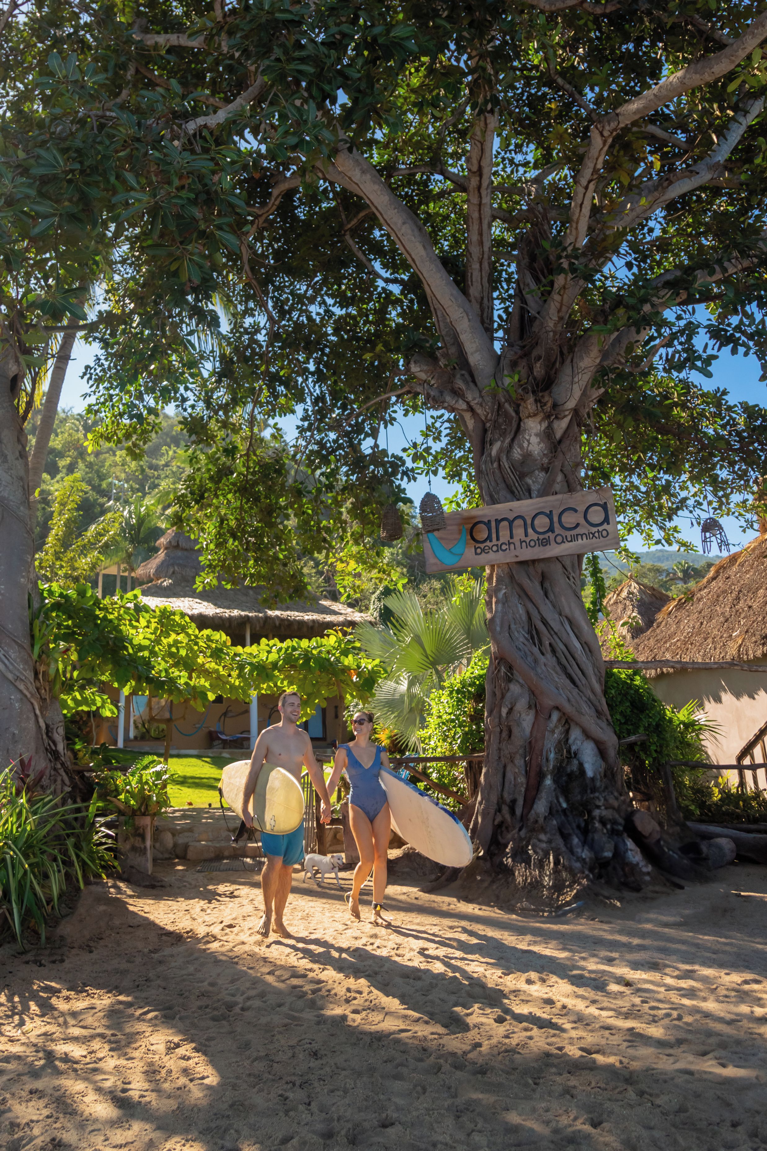 Un camino bordeado de árboles conduce a una zona de playa, con un cartel que dice 'amaca beach hotel Quimudo'.