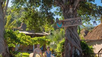 Un camino bordeado de árboles conduce a una zona de playa, con un cartel que dice 'amaca beach hotel Quimudo'.