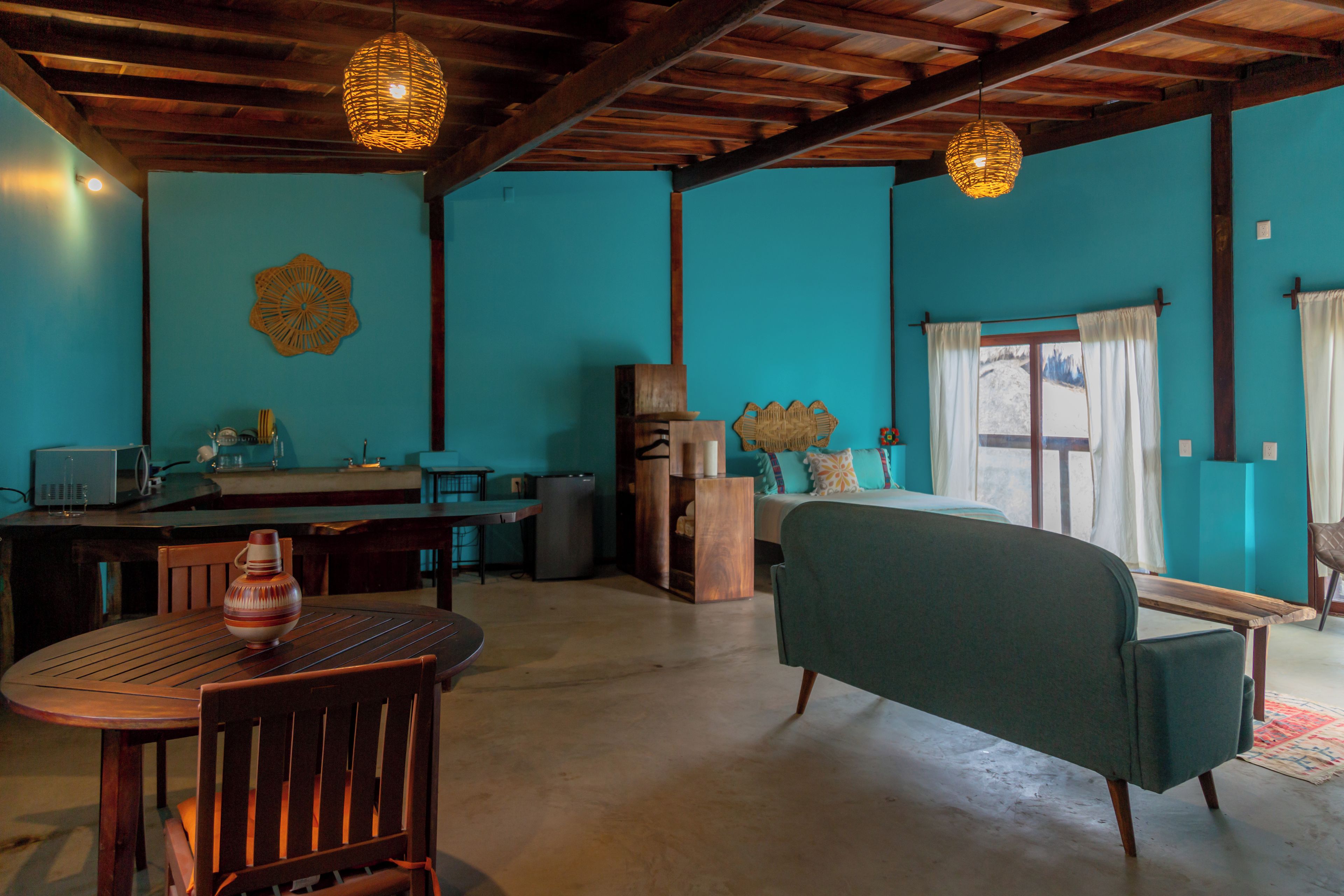 Una habitación con techo de madera, una mesa de comedor con sillas, un sofá y un ventanal con cortinas.