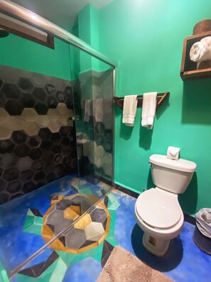 A bathroom with a glass shower enclosure, a toilet, and a patterned floor.
