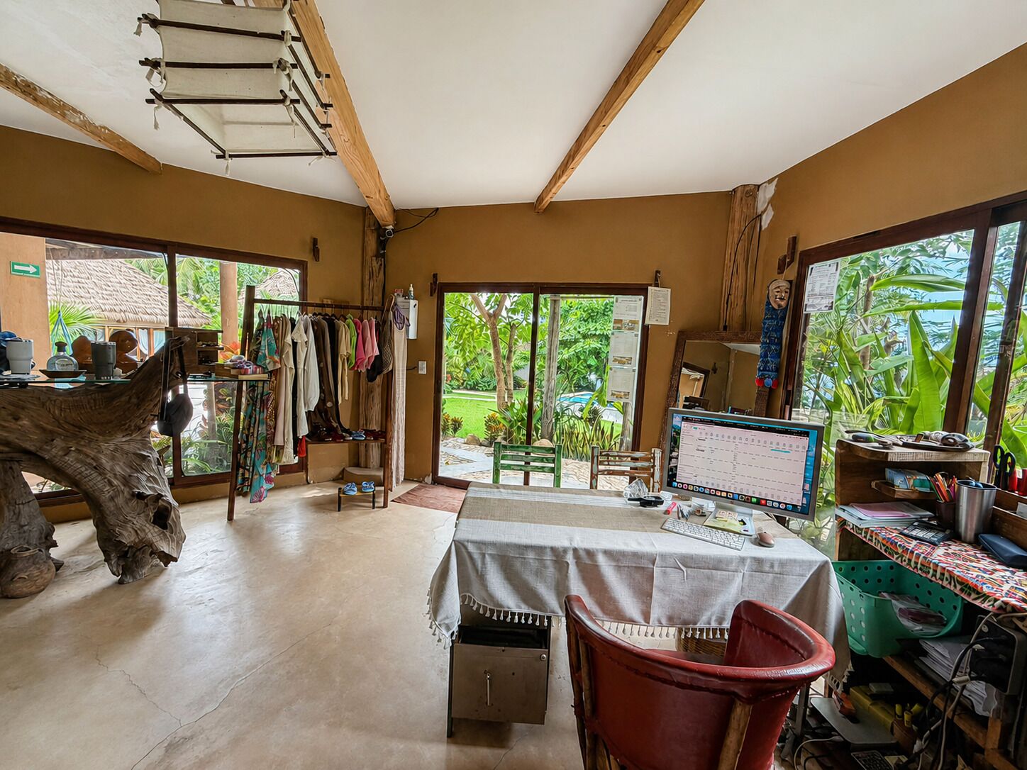 Een kamer met een grote houten tafel, een computer en uitzicht op groen.