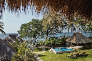 A pool area with a clear view of the ocean, surrounded by lush greenery and thatched-roof structures. - Amaca Beach Retreat - Puerto Vallarta South Shore (Quimixto)