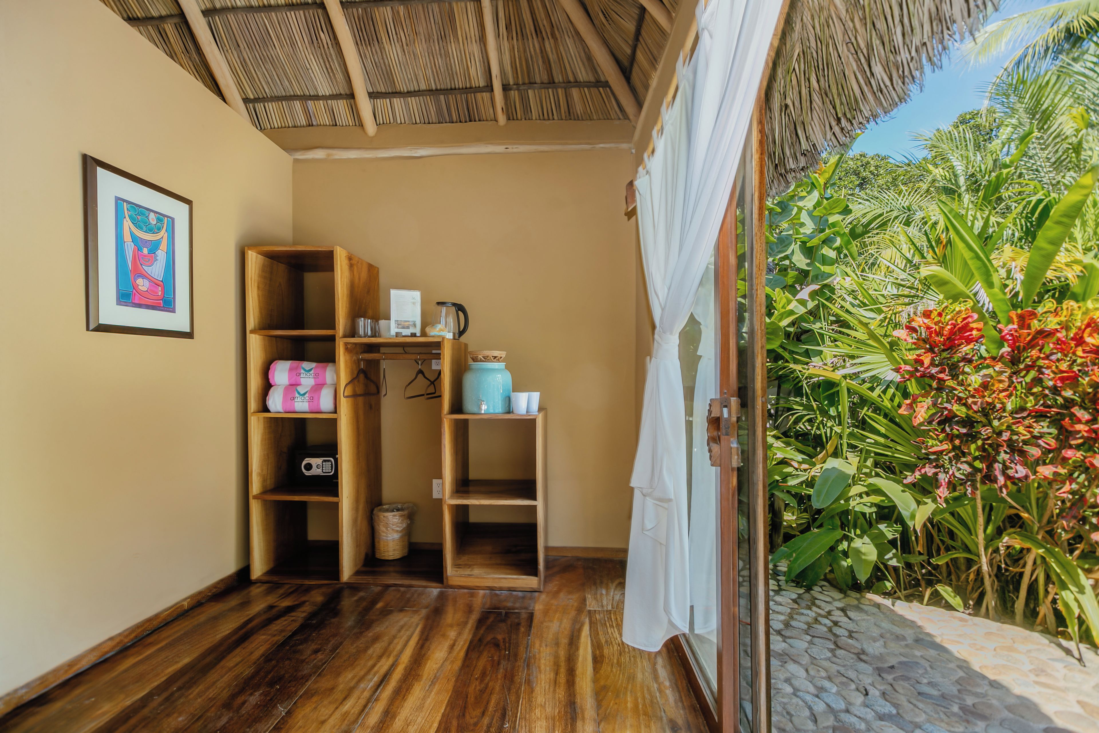 A room with wooden shelves, a framed picture, and a view of tropical plants.