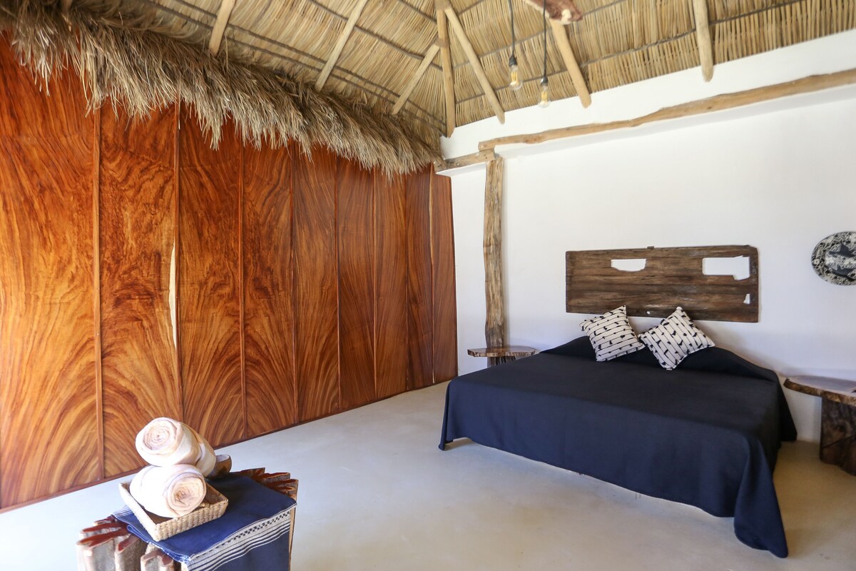 Um quarto com um guarda-roupa de madeira, uma cama com colcha azul escura e uma cesta de vime com toalhas dobradas.