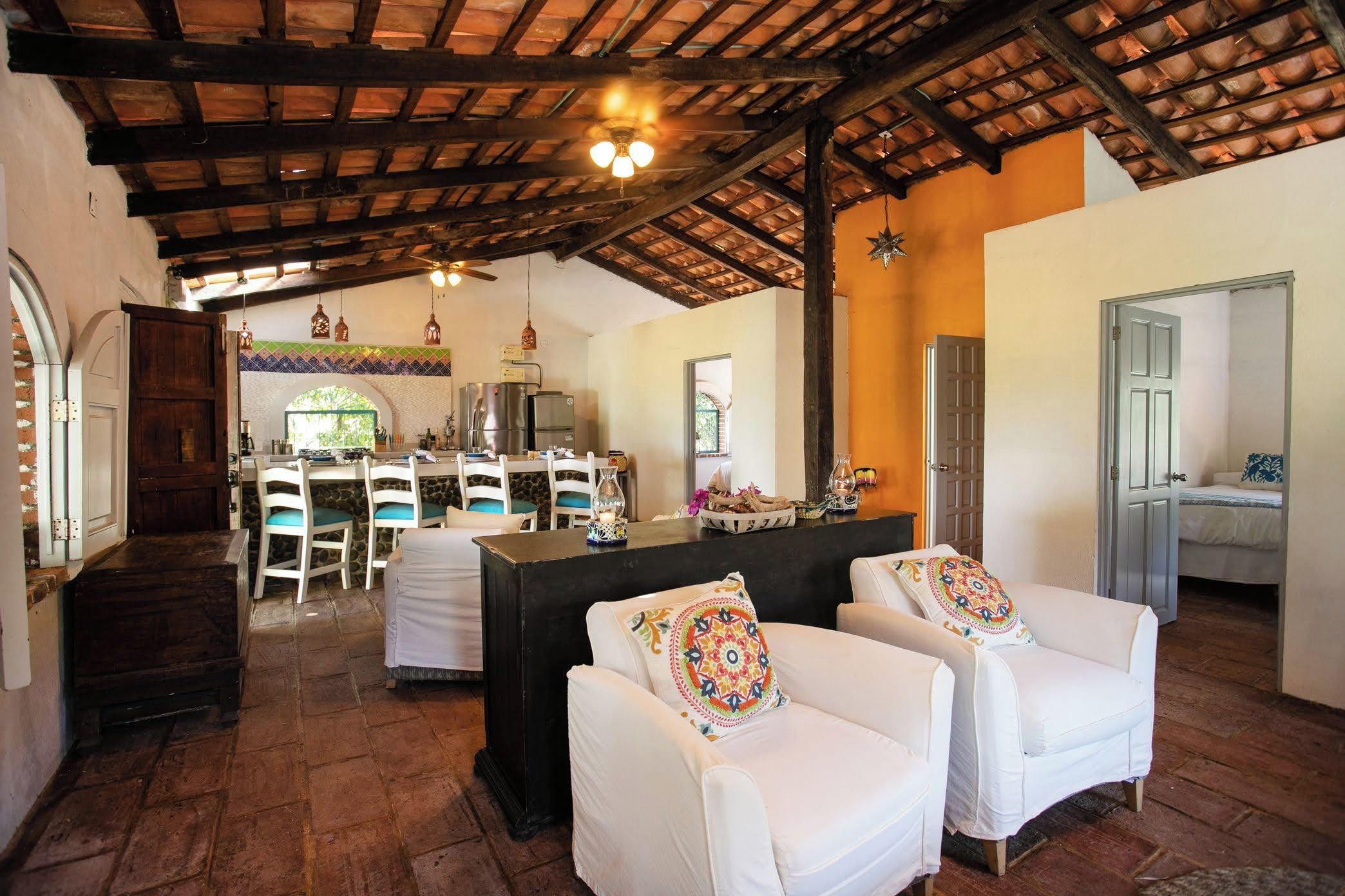 A spacious living area with a high ceiling, a kitchen in the background, and a dining area with white chairs.