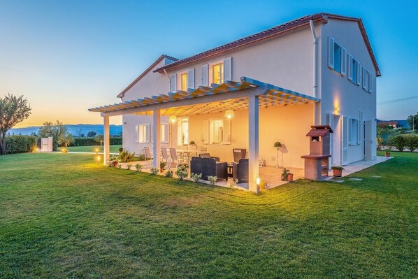 Una casa de dos pisos con un porche cubierto, mobiliario exterior y una chimenea.
