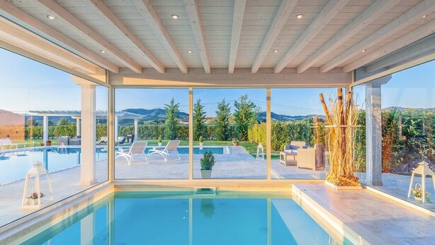 Zona de piscina interior moderna con vistas despejadas a una piscina ajardinada y montañas.