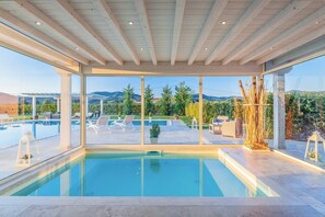 Zona de piscina interior moderna con vistas despejadas a una piscina ajardinada y montañas.