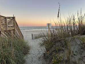 A wooden staircase leading to a beach with sand and grass.
