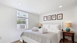 A neatly arranged bedroom with a bed, two bedside tables, a window with blinds, and framed artwork on the wall. - 2BR Sleeps 4 - Beach Retreat  - 100 feet to beach, Walk to Dining & Nightlife (Folly Beach)