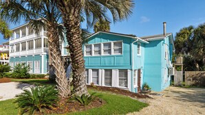 A two-story house with a blue exterior and white trim, surrounded by a gravel driveway and palm trees. - 2BR Sleeps 4 - Beach Retreat  - 100 feet to beach, Walk to Dining & Nightlife (Folly Beach)