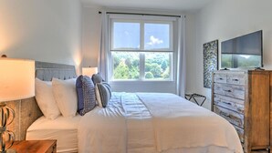 Camera da letto con un letto grande, una ventola a soffitto, una finestra con vista sul verde, un comò di legno e una TV a schermo piatto.
