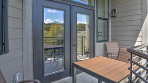 Patio esterno moderno con porta scorrevole in vetro che dà su un balcone, un tavolo in legno e due sedie.