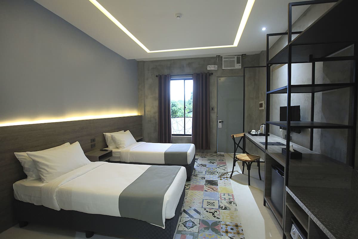 A hotel room with two beds, a desk, a chair, and a TV.